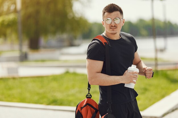 Mężczyzna stojący nad wodą. Facet w sportowym ubraniu. Mężczyzna w letnim parku z plecakiem