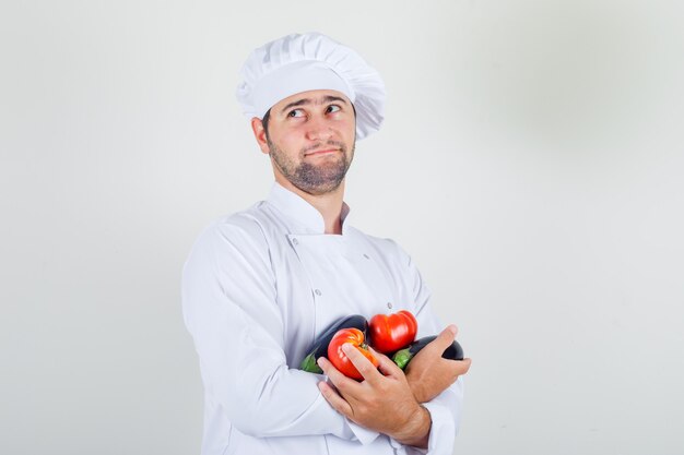 Mężczyzna szefa kuchni w białym mundurze, trzymając pomidory i bakłażan