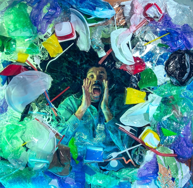 Mężczyzna tonący w wodzie pod stosem pojemników z tworzyw sztucznych, śmieci. Używane butelki i opakowania napełniające światowe oceany zabijające ludzi.