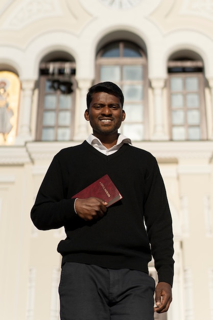 Bezpłatne zdjęcie mężczyzna trzymający książkę biblijną przed kościołem