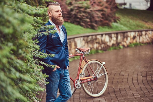 Mężczyzna ubrany w codzienny strój, stojący z retro rowerem w miejskim parku.