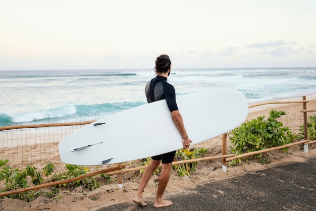 Bezpłatne zdjęcie mężczyzna ubrany w ubrania surferów i trzymając jego deskę surfingową z daleka