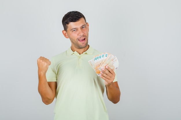 Mężczyzna unoszący zaciśniętą pięść z banknotami w koszulce i wyglądający na szczęśliwego