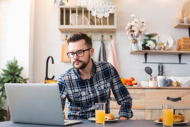 Mężczyzna używa laptop przy śniadaniowym stołem