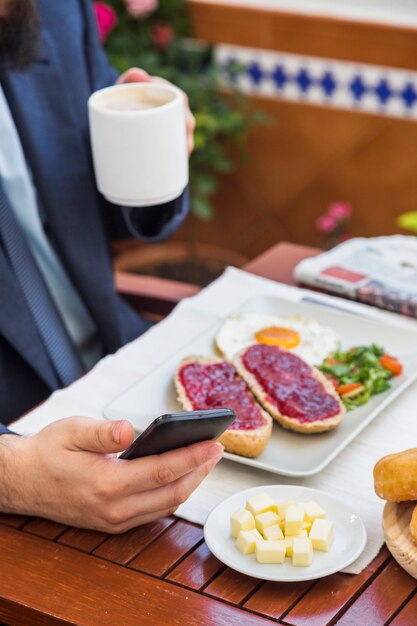 Mężczyzna używa telefon komórkowego podczas gdy pijący filiżankę kawy