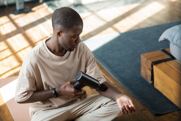 Bezpłatne zdjęcie mężczyzna używający pistoletu do masażu na ramieniu pod wysokim kątem
