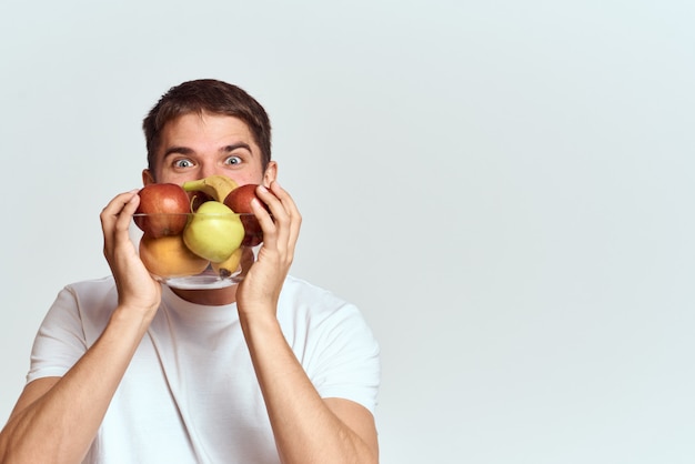 Mężczyzna w białej koszulce ze zdrowymi warzywami i owocami w rękach