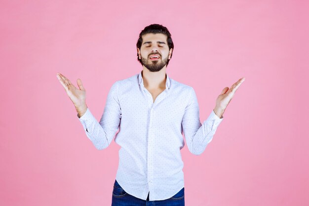 Mężczyzna w białej koszuli podnosi rękę, aby zwrócić na siebie uwagę lub coś pokazać.