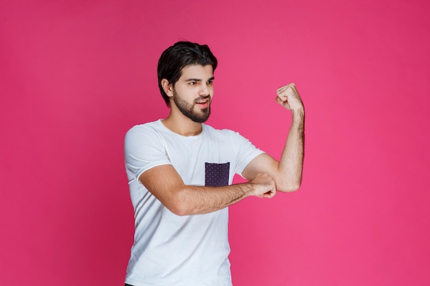 Mężczyzna w białej koszuli pokazując mięśnie pięści i bicepsa.