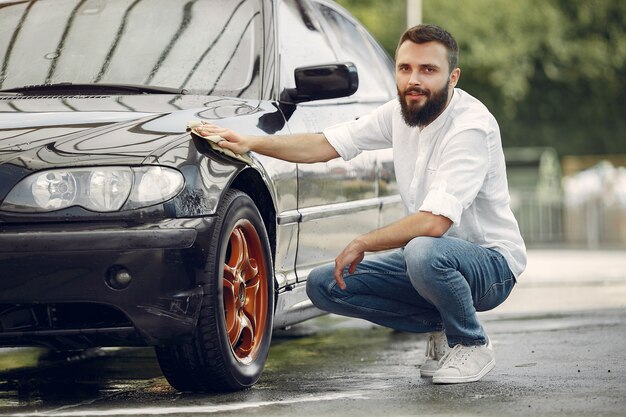 Mężczyzna w białej koszuli wyciera samochód w myjni samochodowej