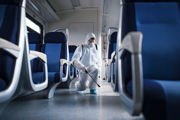 Mężczyzna w białym kombinezonie ochronnym dezynfekujący i dezynfekujący wnętrze pociągu metra, aby powstrzymać rozprzestrzenianie wysoce zaraźliwego wirusa koronowego