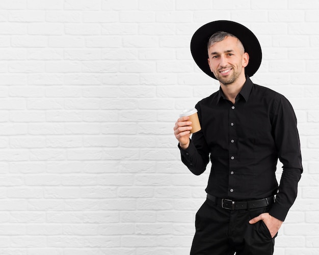 Bezpłatne zdjęcie mężczyzna w czarnym garniturze na sobie kapelusz i trzyma kawę