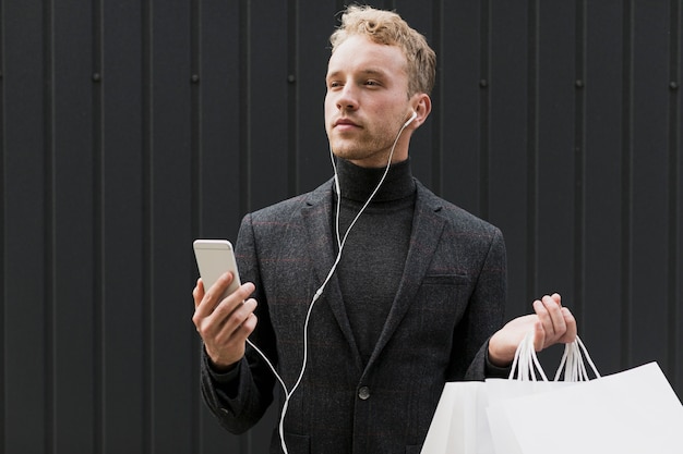 Bezpłatne zdjęcie mężczyzna w czerni z torba na zakupy i smartphone