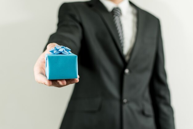 Mężczyzna w garniturze posiadający małe niebieskie pudełko na prezent