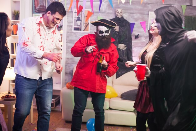 Mężczyzna w kostiumie pirata trzymający piwo na obchodach halloween z przyjaciółmi.