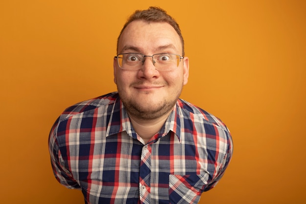 Bezpłatne zdjęcie mężczyzna w okularach i koszuli w kratkę uśmiechnięty z szczęśliwą twarzą stojącą nad pomarańczową ścianą