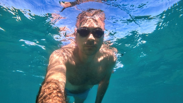 Mężczyzna w okularach pływających pod błękitną i przejrzystą wodą Morza Śródziemnego. Trzymanie aparatu