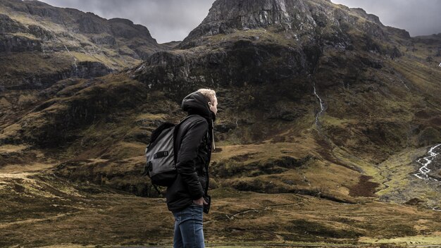 Mężczyzna w plecaku i ciepły płaszcz idący po górach Szkocji pod szarym niebem
