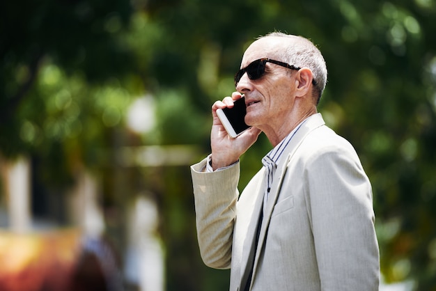 Mężczyzna w średnim wieku rasy białej w okularach rozmawia na smartfonie na ulicy