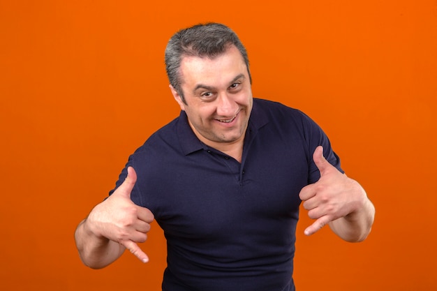 Mężczyzna w średnim wieku ubrany w koszulkę polo na pokazie pozwala pić gesty, uśmiechając się nad odosobnioną pomarańczową ścianą