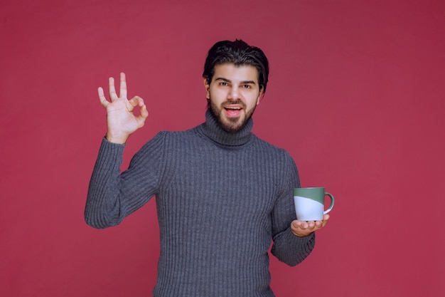Mężczyzna w szarym swetrze trzyma kubek kawy i cieszy się smakiem.