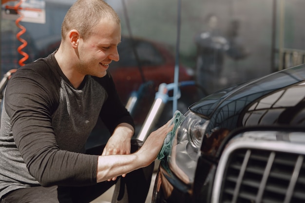 Mężczyzna W Szarym Swetrze Wyciera Samochód W Myjni Samochodowej