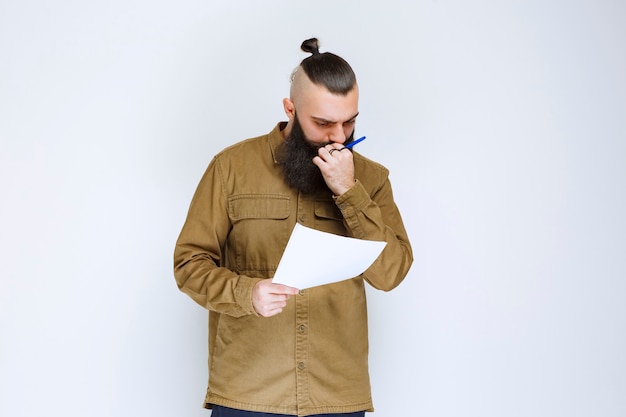 Mężczyzna z brodą sprawdzający listę projektów i zaznaczający notatki lub poprawki.