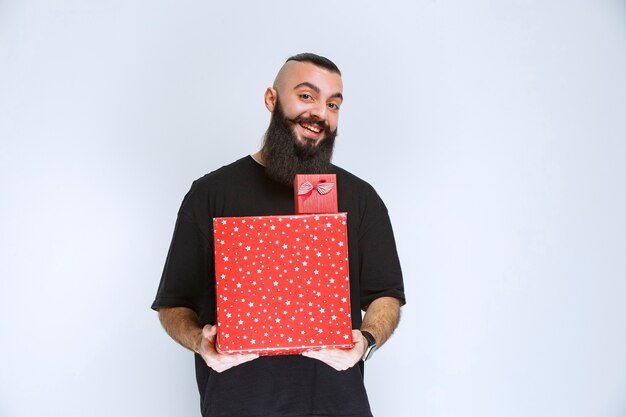 Mężczyzna z brodą trzymający czerwone pudełka na prezenty i oferujący go swojej dziewczynie.