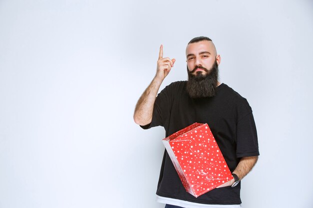 Mężczyzna z brodą, trzymający czerwone pudełka na prezenty i wahający się, czy dokonać wyboru.