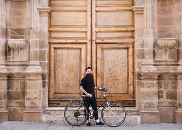 Mężczyzna z rowerową pozycją przed zamkniętą wielką rocznika drewnianą ścianą