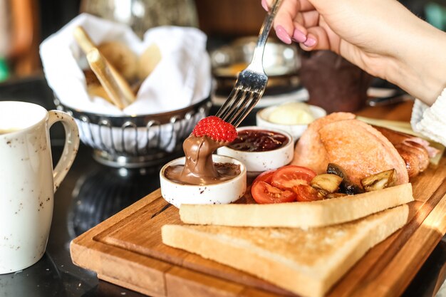 Mężczyzna zanurza truskawkę w czekoladowym maśle zestaw śniadaniowy toast pomidorowy miód widok z boku