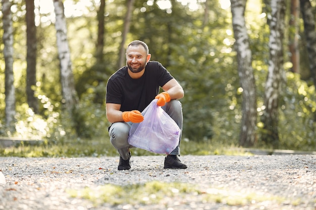 Mężczyzna zbiera śmieci w workach na śmieci w parku