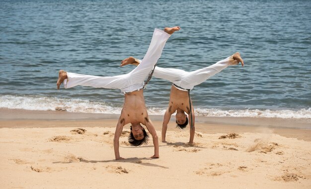Mężczyźni bez koszuli ćwiczący capoeira na plaży