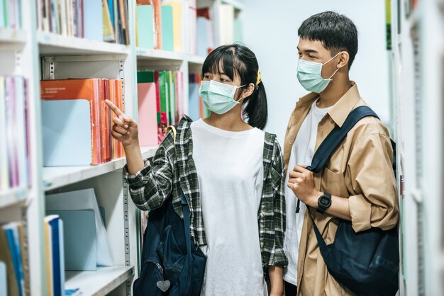 Mężczyźni i kobiety niosący plecak i szukający książek w bibliotece.