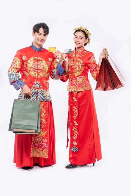 Bezpłatne zdjęcie mężczyźni i kobiety noszą qipao, noszą papierowe torby, chodzą na zakupy z kartą kredytową.