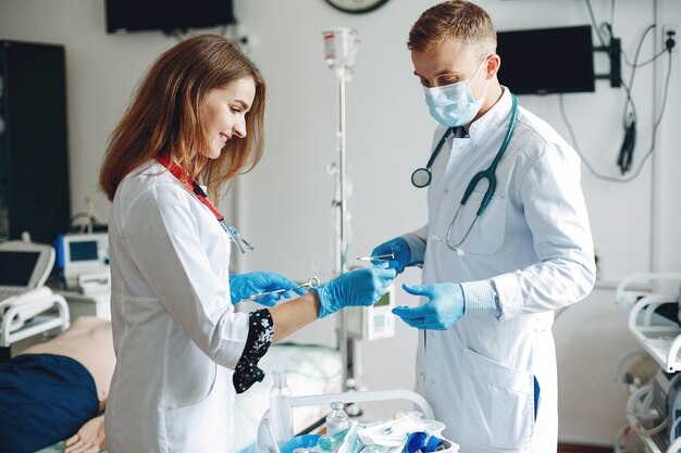 Mężczyźni i kobiety w szpitalnych togach trzymają w rękach sprzęt medyczny. Pielęgniarka wybiera lek do wstrzyknięcia.