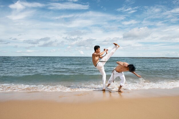 Mężczyźni na plaży ćwiczący razem capoeirę