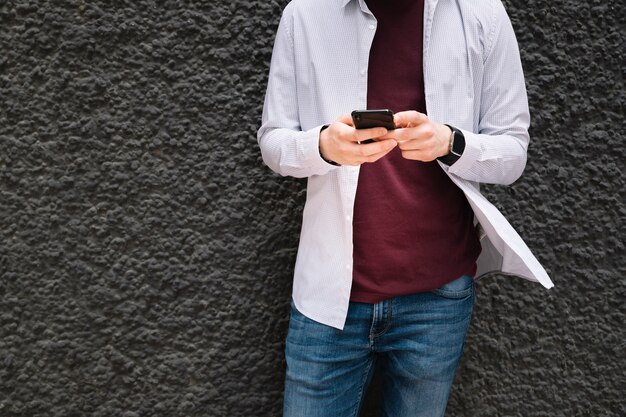 Bezpłatne zdjęcie midsection mężczyzna opiera na ściennym używa telefonie komórkowym