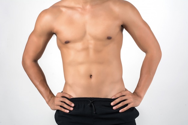 Mięśniowy mężczyzna pokazuje sześć paczek abs odizolowywających na białym tle.