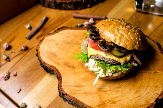 Mięsny hamburger na drewnianej deski coleslaw ogórkowych pomidorowych pieczarek serowym bocznym widoku