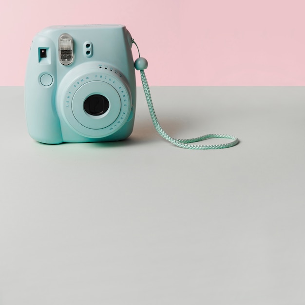 Mini niebieska błyskawiczna kamera na szarym biurku na różowym tle