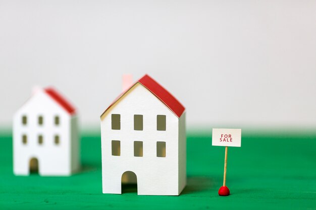 Miniaturowy dom model blisko sprzedaży etykietki na zielonym textured biurku przeciw białemu tłu