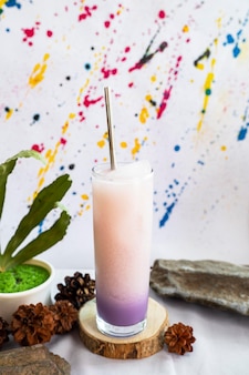 Minimalistyczny pomysł na koncepcję. fioletowy napój lód mleka sodowego na kamieniu z zielonymi liśćmi na streszczenie tło.