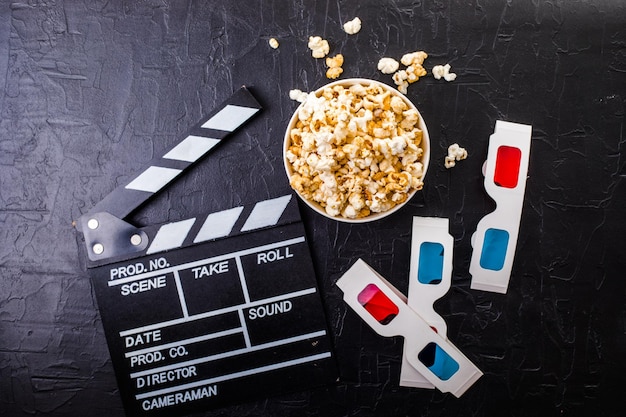 Minimalna koncepcja kina. popcorn, 3d okulary klapy deska na czarnym tle. płaski układanie, widok z góry