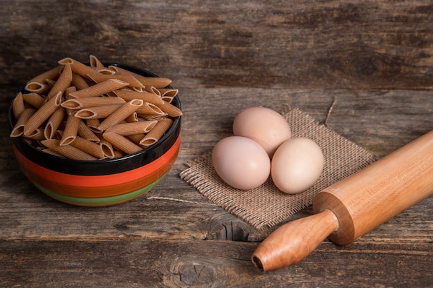 Miska Surowego Makaronu Penne I Jaj Na Powierzchni Drewnianych. Wysokiej Jakości Zdjęcie