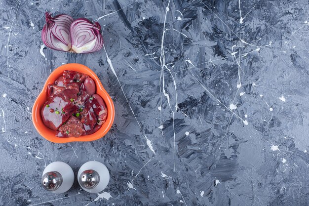 Miska wątróbek drobiowych obok cebuli, soli i pieprzu na niebieskim stole.