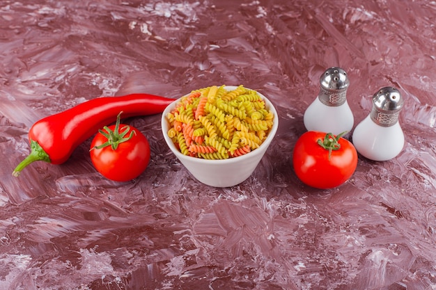 Miska Wielobarwnego Surowego Makaronu Spirali Ze świeżymi Czerwonymi Pomidorami I Papryczką Chili.