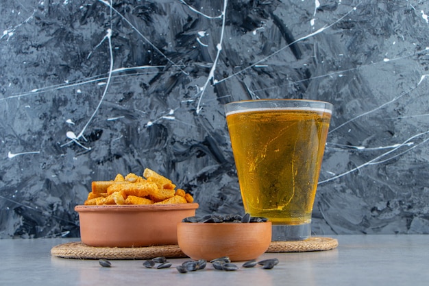 Miska z grzankami i nasionami obok piwa w szklance, na marmurowym tle.