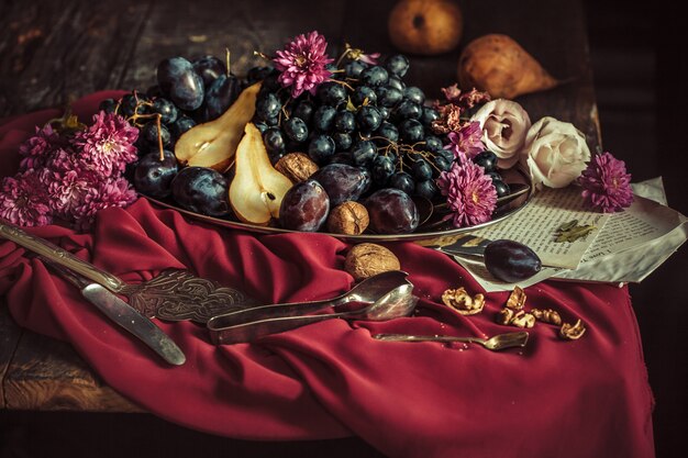 Miska z winogronami i śliwkami na bordowym obrusie