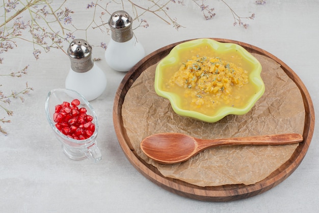 Bezpłatne zdjęcie miska zupy na drewnianym talerzu z solą i nasionami granatu.